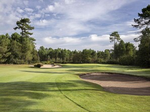 Ein Golfplatz mit Sandbunkern, einer Fahne und blauem Himmel.