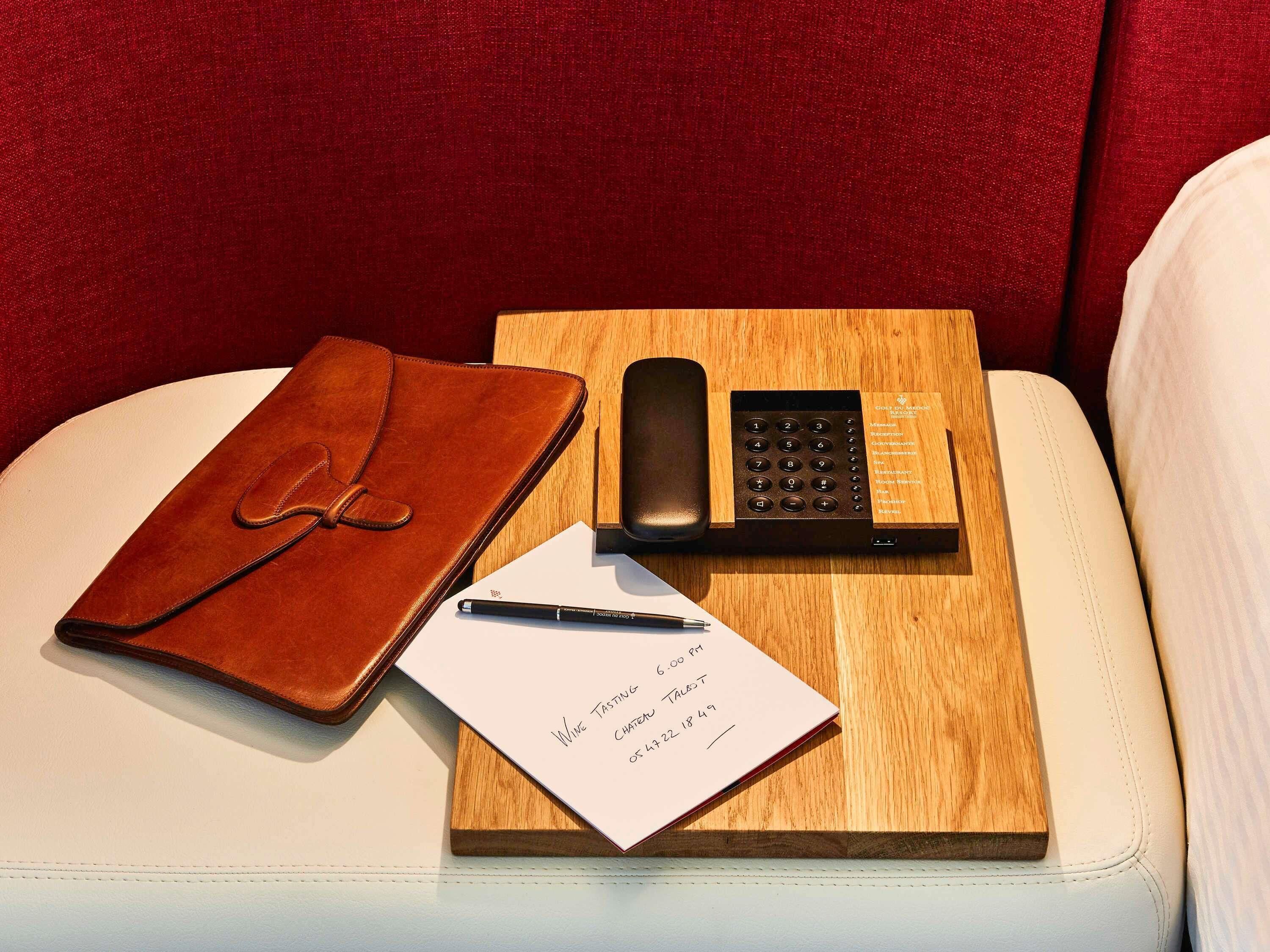 A leather notebook, a pen, a smartphone, and a notepad with handwritten notes on a wooden tray.
