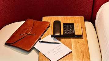 A leather notebook, a pen, a smartphone, and a notepad with handwritten notes on a wooden tray.