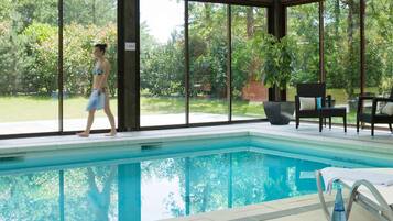 An indoor swimming pool with clear glass walls, a tiled floor, and a potted plant.