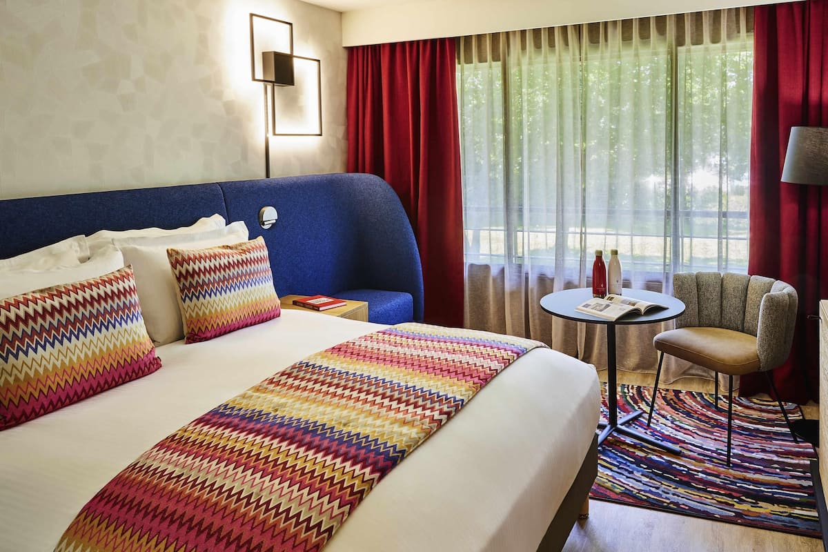 A hotel room with a large bed, a blue headboard, a small round table, and a chair.