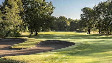 Een golfbaan met zandbunkers, bomen en een heldere lucht.
