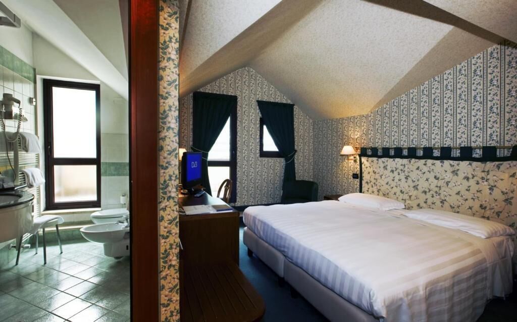 A bedroom with a bed, a desk with a computer, a chair, and a window.