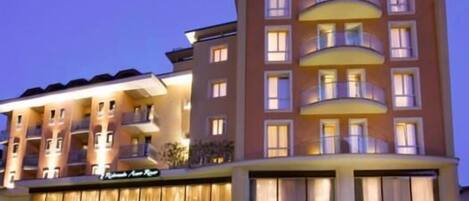 Un hotel de varios pisos con balcones, entrada a nivel de calle y un letrero que indica que es un hotel.