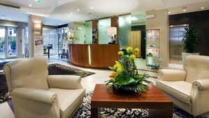 A hotel lobby with a reception desk, two sofas, a coffee table with flowers, and a large window. - Rizzi Aquacharme Hotel & Spa (Darfo Boario Terme)