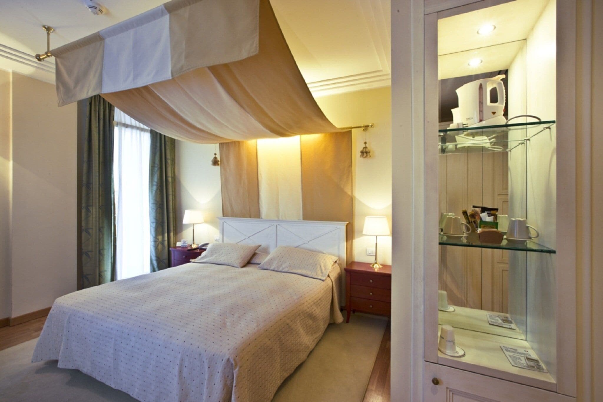 Une chambre d’hôtel avec un grand lit, une armoire en verre contenant des articles de toilette et une table de chevet avec une lampe.