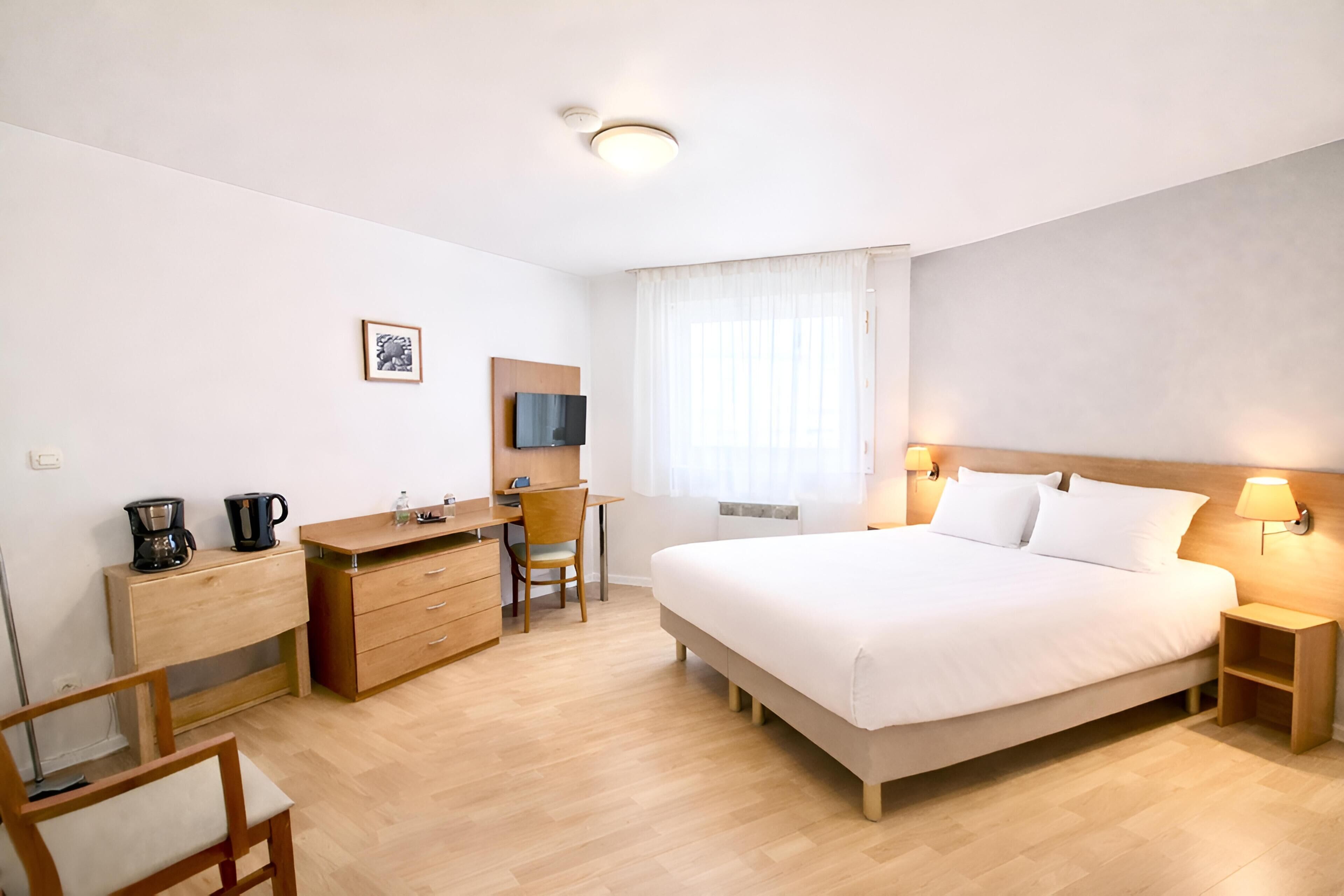 A hotel room with a bed, desk, chair, and a television.