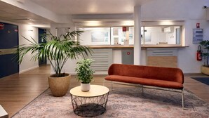 Eine moderne Lobby mit einer Couch, zwei Blumentöpfen, einem runden Tisch und einer Rezeption.