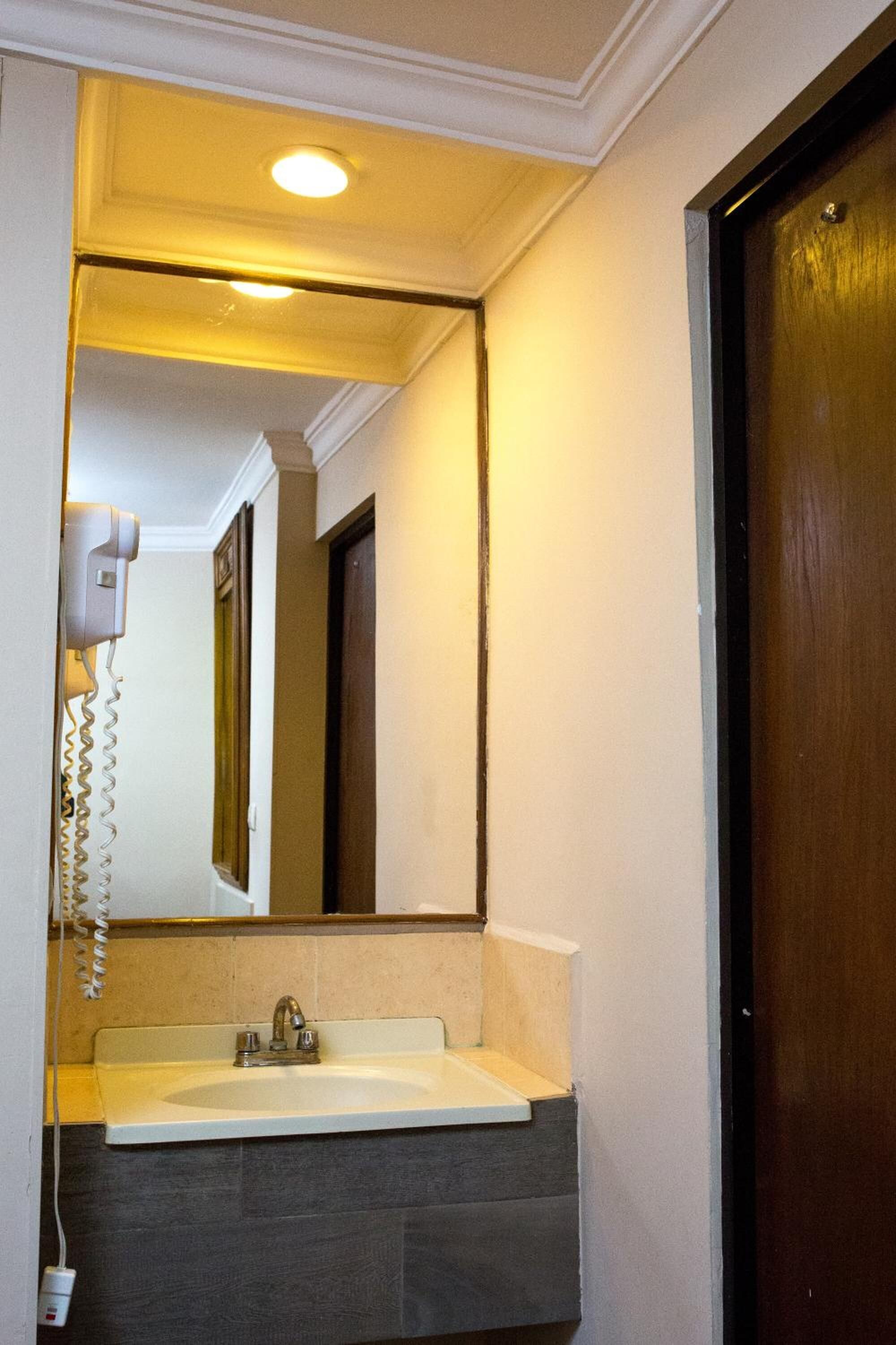 A bathroom with a sink, mirror, and a hairdryer on the wall.