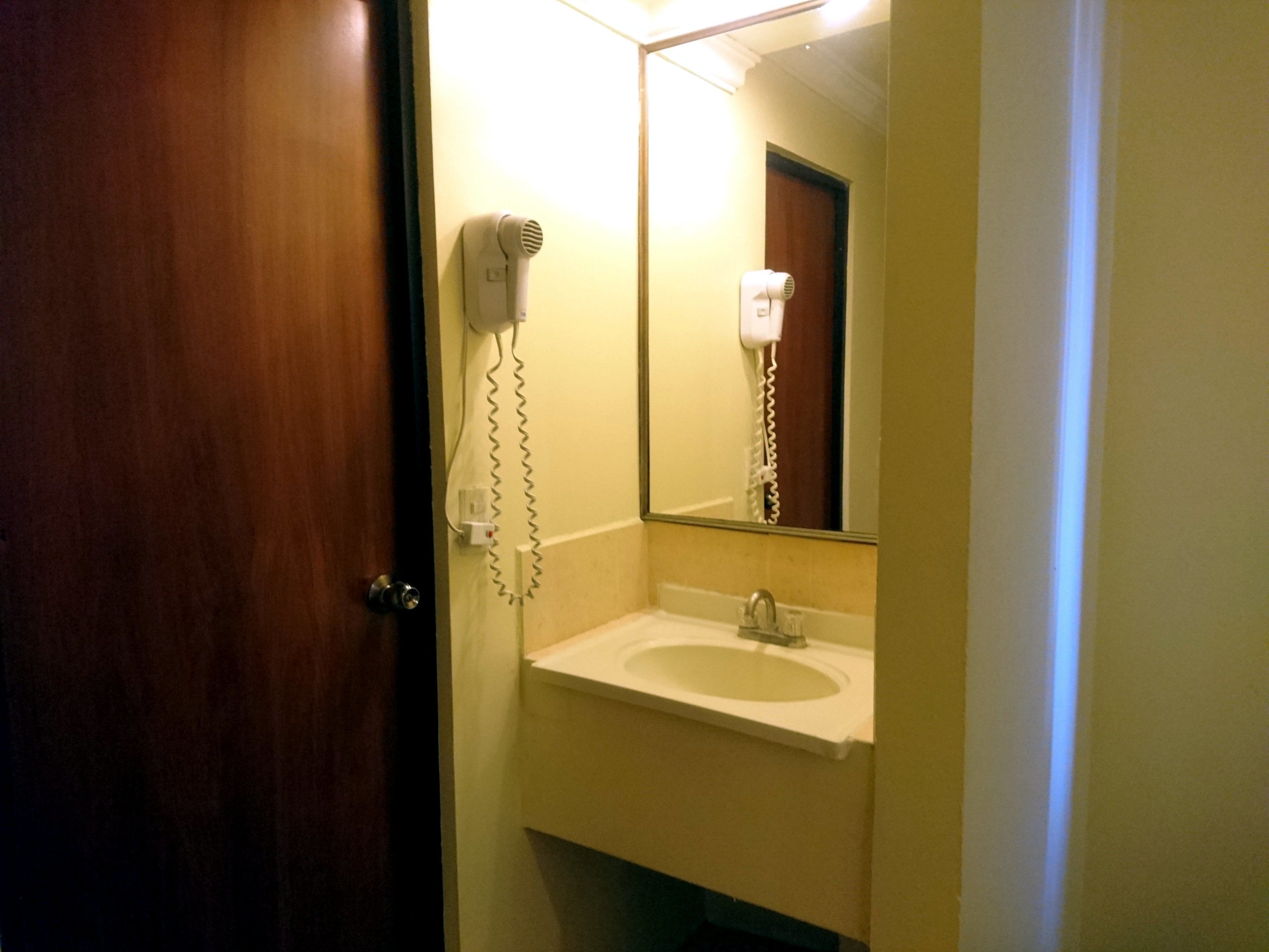 A bathroom with a sink, a mirror, and a hairdryer mounted on the wall.