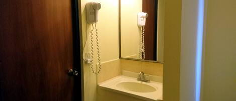 A bathroom with a sink, a mirror, and a hairdryer mounted on the wall.