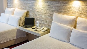 Hotellihuone, jossa on kaksi sänkyä, työpöytä, jossa on kannettava tietokone, puhelin ja kuppi.