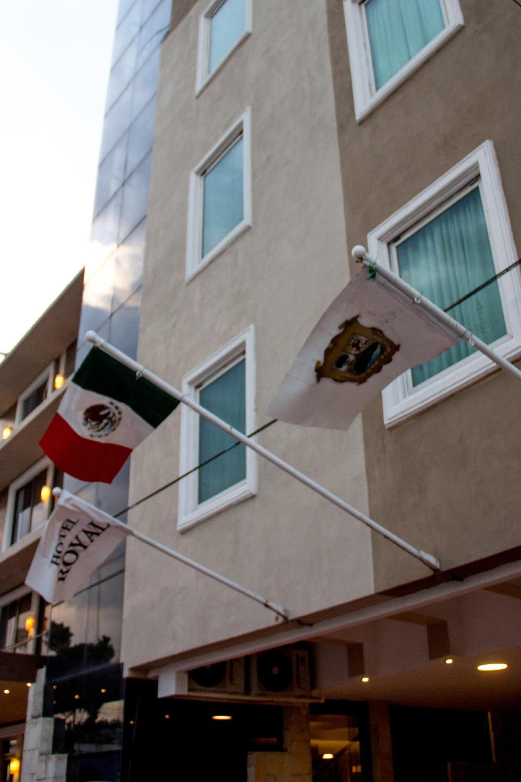 A hotel building with multiple windows and flags, including the Mexican flag and a flag with a coat of arms.