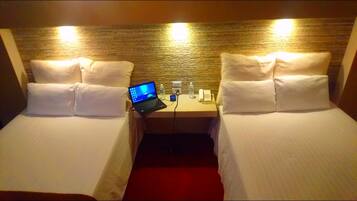A hotel room with two single beds, a desk with a laptop, a phone, and a water bottle.