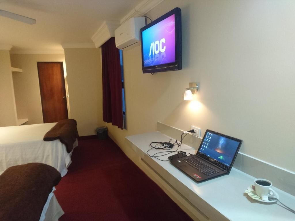 Een hotelkamer met twee bedden, een televisie, een bureau met een laptop en een kop koffie.