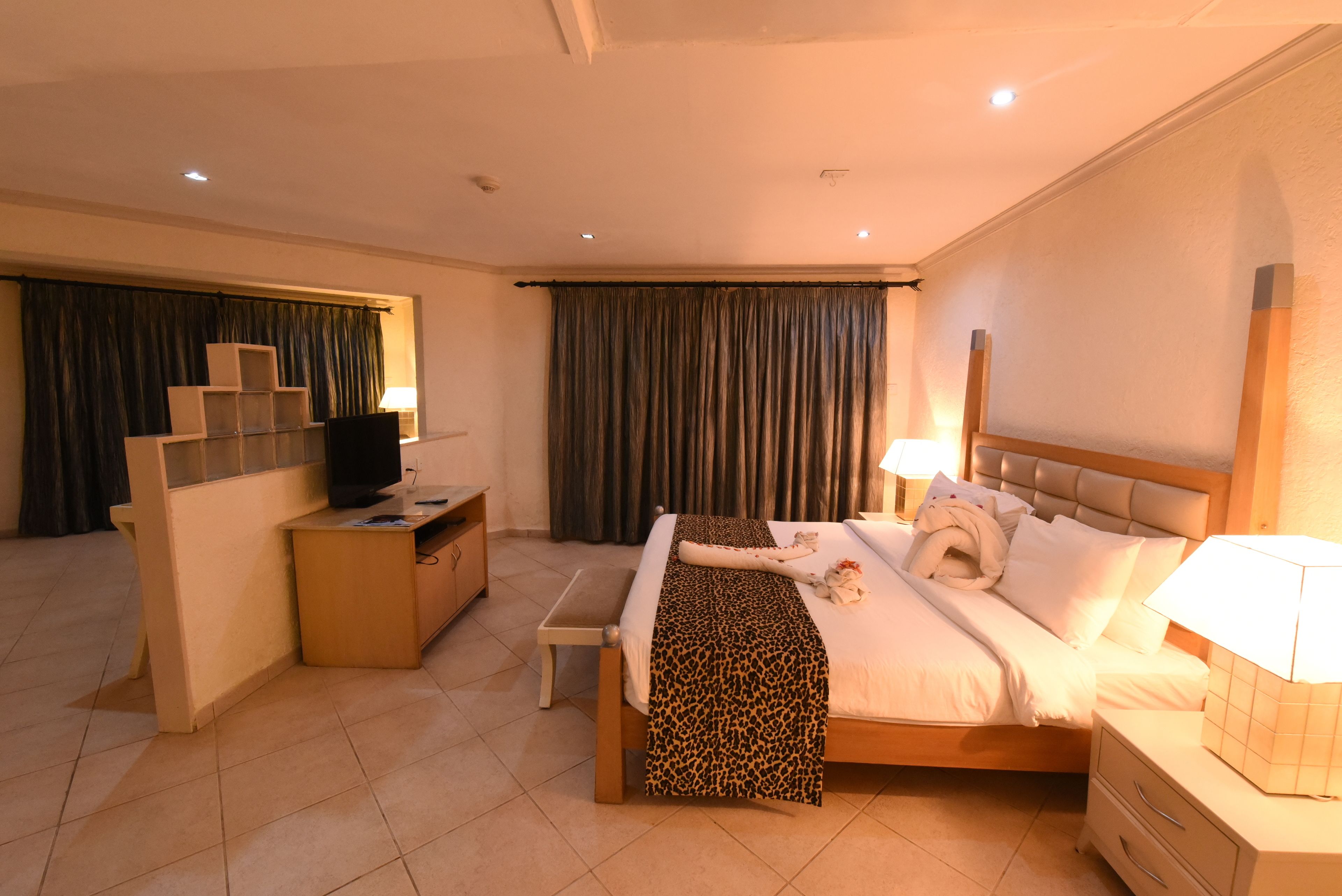 A hotel room with a bed, bedside tables, a desk, a television, and curtains.