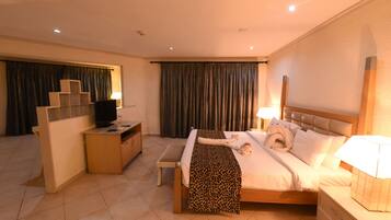 A hotel room with a bed, bedside tables, a desk, a television, and curtains.