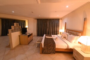 A hotel room with a bed, bedside tables, a desk, a television, and curtains.