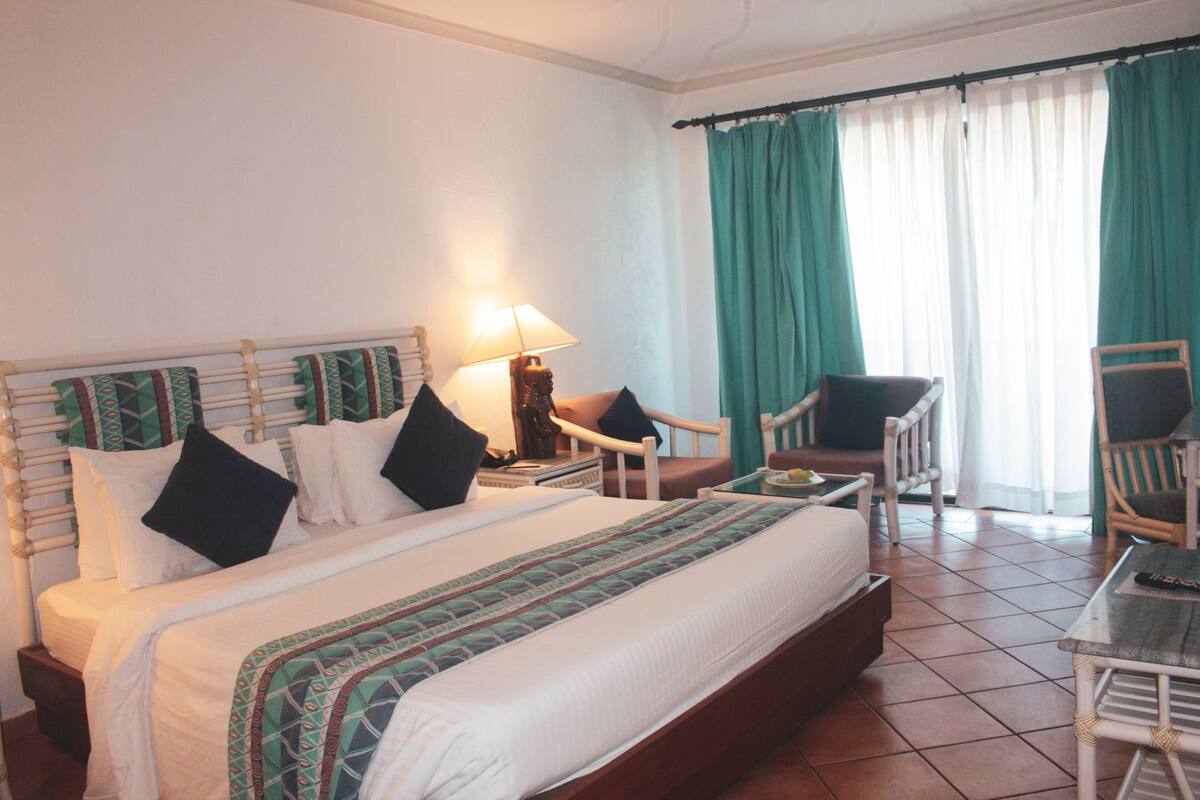 A hotel room with a large bed, two chairs, a small table, and a window with curtains.