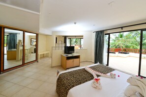 Ein Hotelzimmer mit einem großen Bett, einem Schreibtisch mit Fernseher, einem Spiegel und einem Balkon mit Blick auf Palmen.