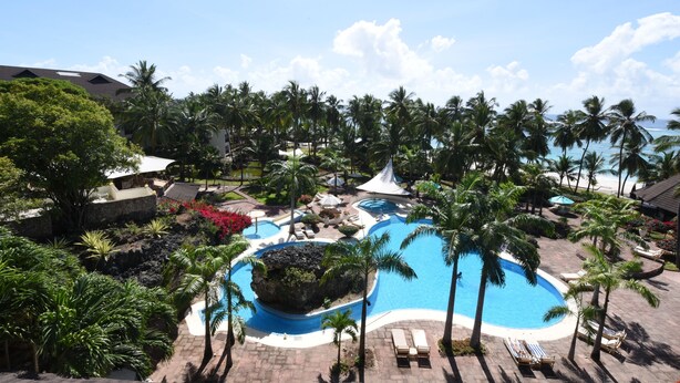 A resort with a central swimming pool surrounded by palm trees and lounge chairs. - Diani Reef Beach Resort & Spa - Your Beachfront Bliss Awaits (Diani Beach)