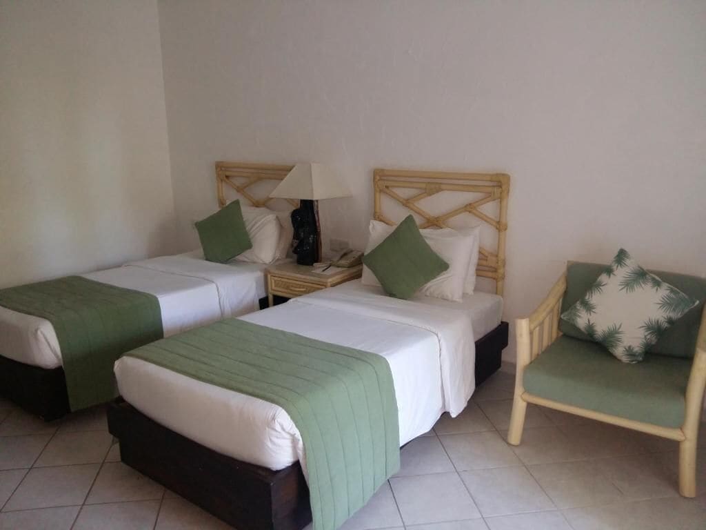 A hotel room with two single beds, a chair, and a nightstand with a lamp.
