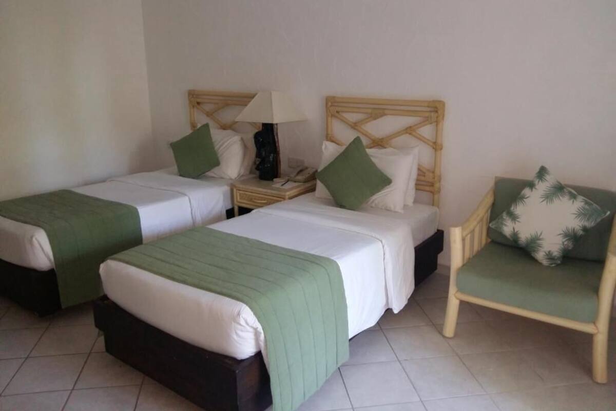 A hotel room with two single beds, a chair, and a nightstand with a lamp.