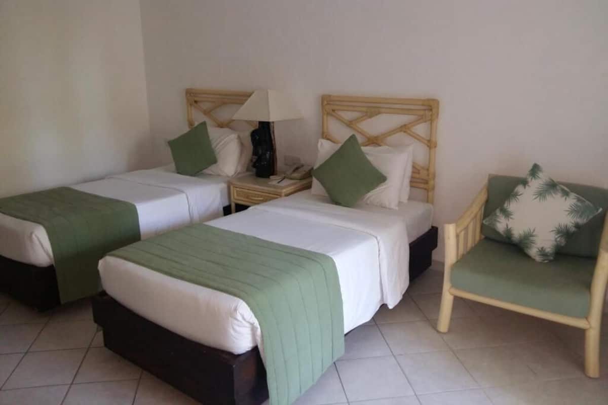 A hotel room with two single beds, a chair, and a nightstand with a lamp.