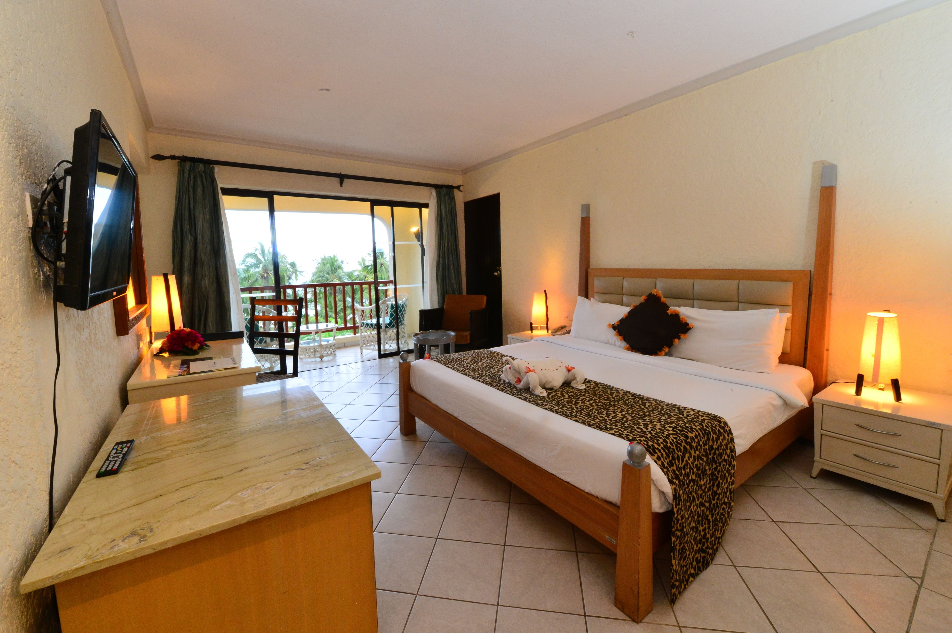 A hotel room with a bed, a desk, a TV, a balcony, and a nightstand.