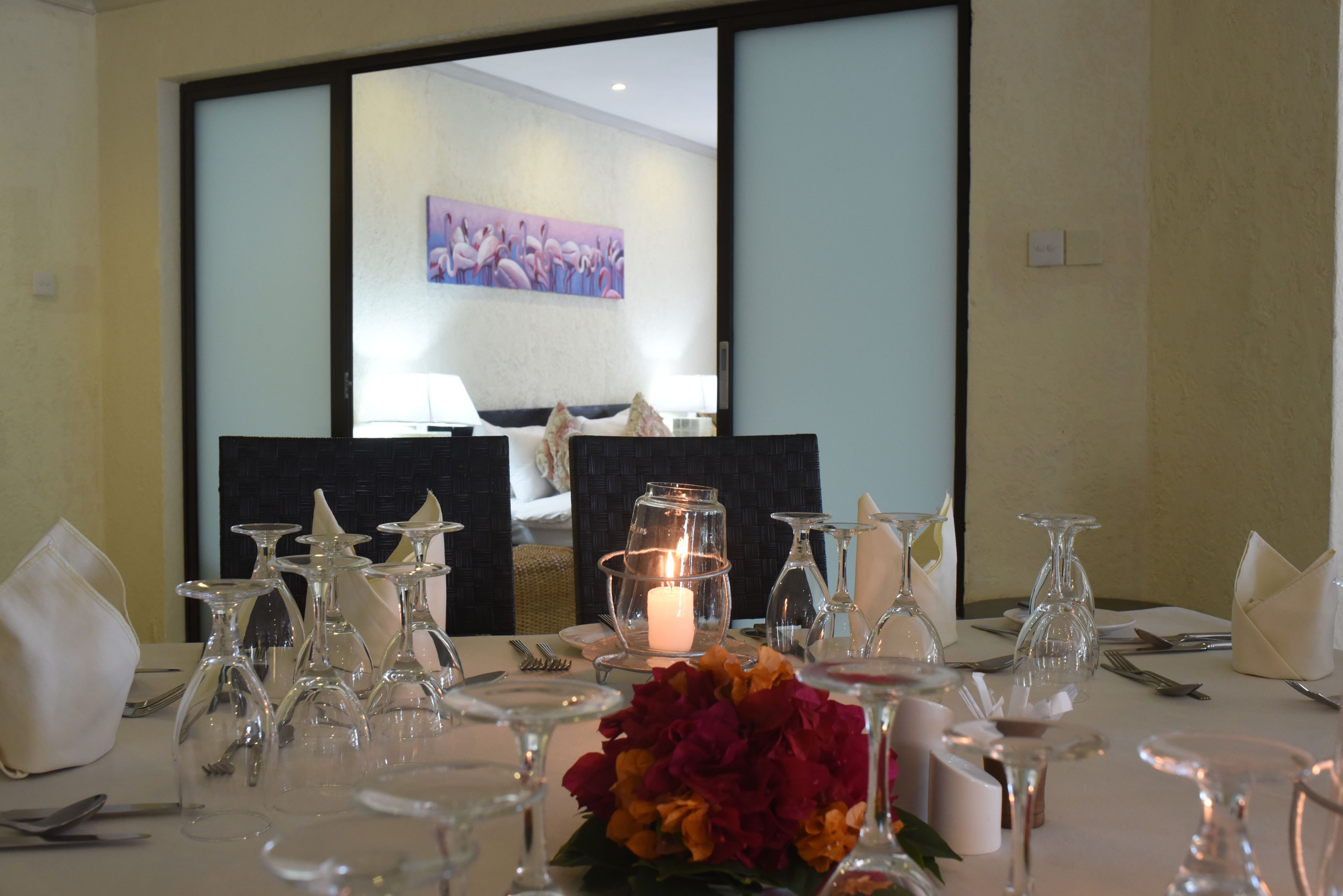 A hotel room with a dining table set for a meal, a lit candle centerpiece, and a painting on the wall.