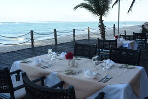A table set for dining with a view of the ocean, equipped with wicker chairs and a white tablecloth.