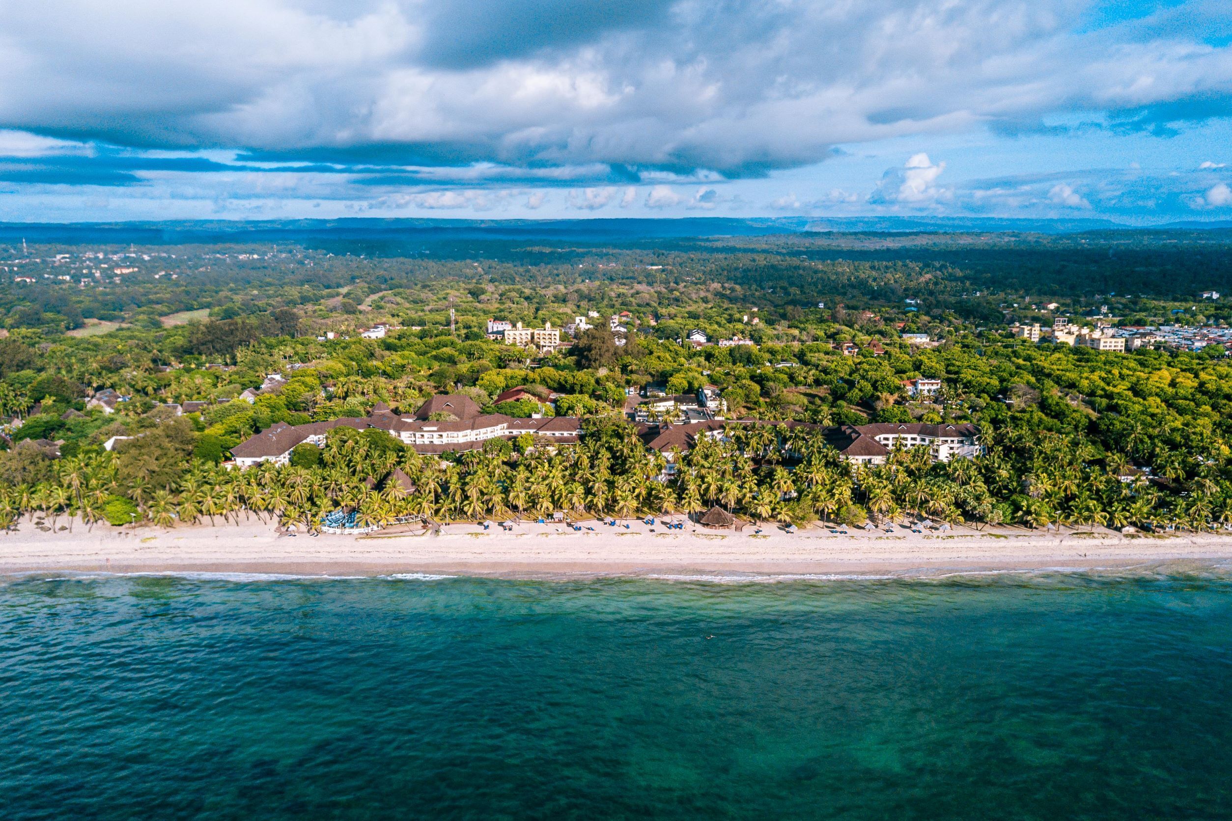 An aerial view of a coastal area with a beach, houses, and dense greenery.