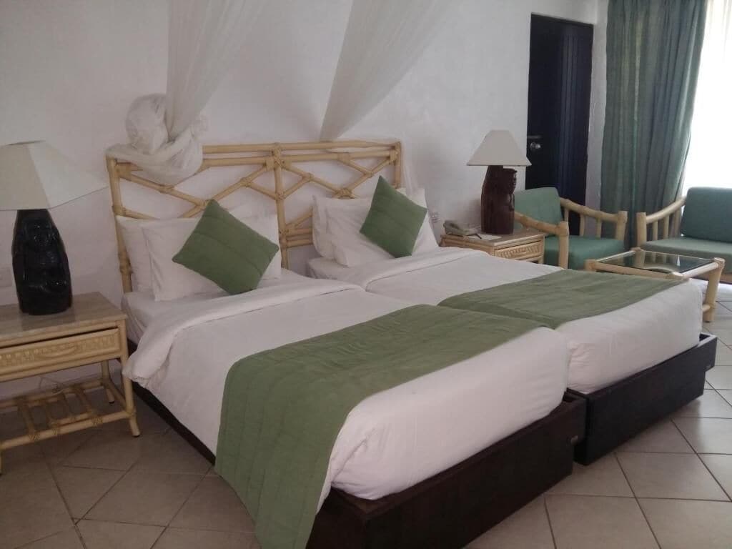 A double bed with a green bedspread, two nightstands with lamps, a chair, and a bedside table.