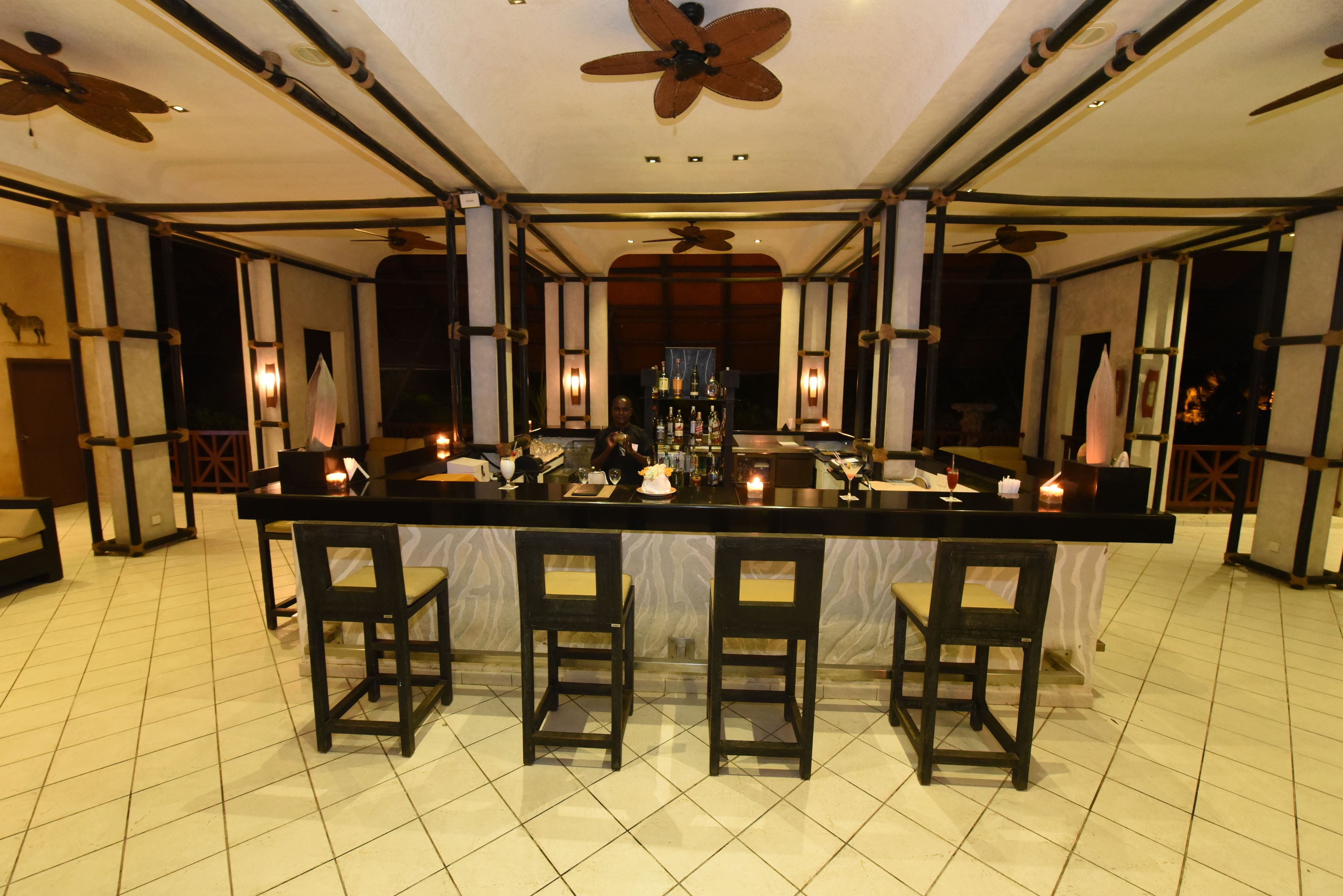 Uma área de bar com um balcão comprido, várias cadeiras e ventiladores de teto.