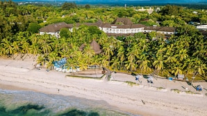 An aerial view of a resort with multiple buildings surrounded by palm trees, a beach, and ocean views. - Diani Reef Beach Resort & Spa - Your Beachfront Bliss Awaits (Diani Beach)