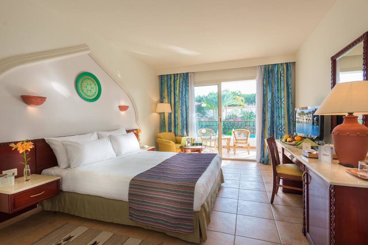 A hotel room with a bed, a desk, a chair, a TV, and a balcony with curtains.