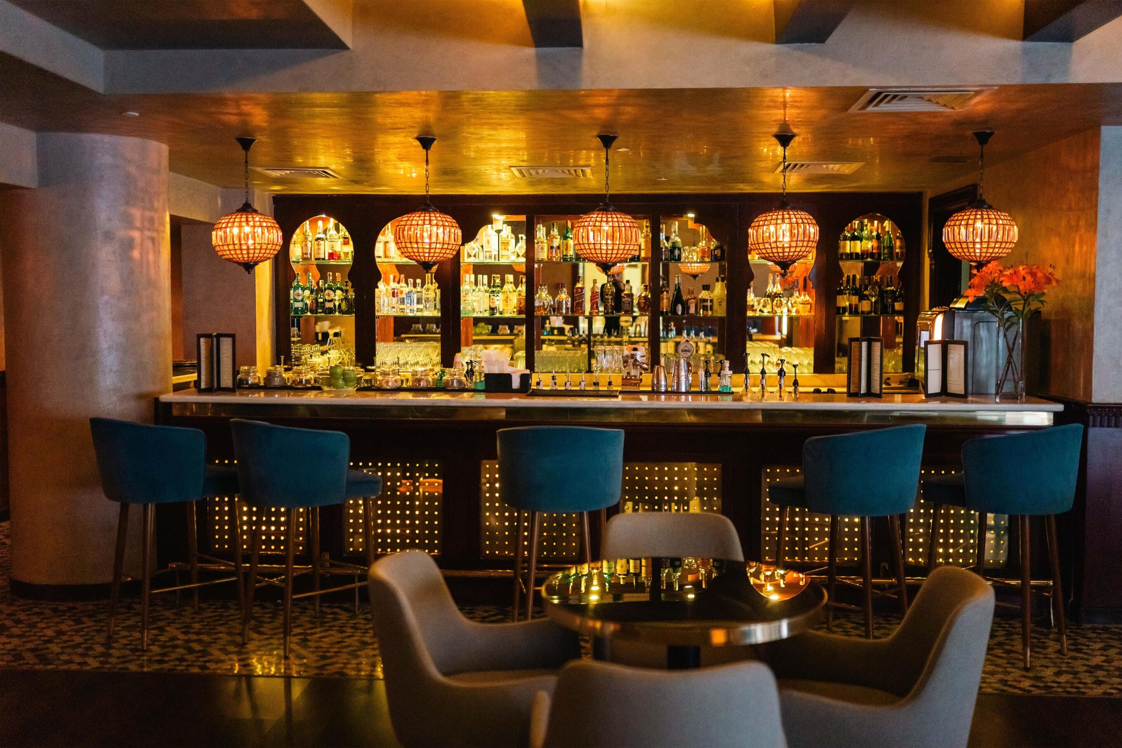 A bar area with multiple hanging light fixtures, a bar counter, and several chairs.
