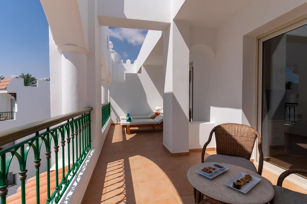 A balcony with a green railing, a wicker chair, a small table with plates, and a sofa with cushions.