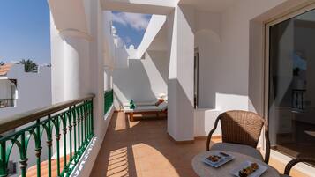 A balcony with a green railing, a wicker chair, a small table with plates, and a sofa with cushions.