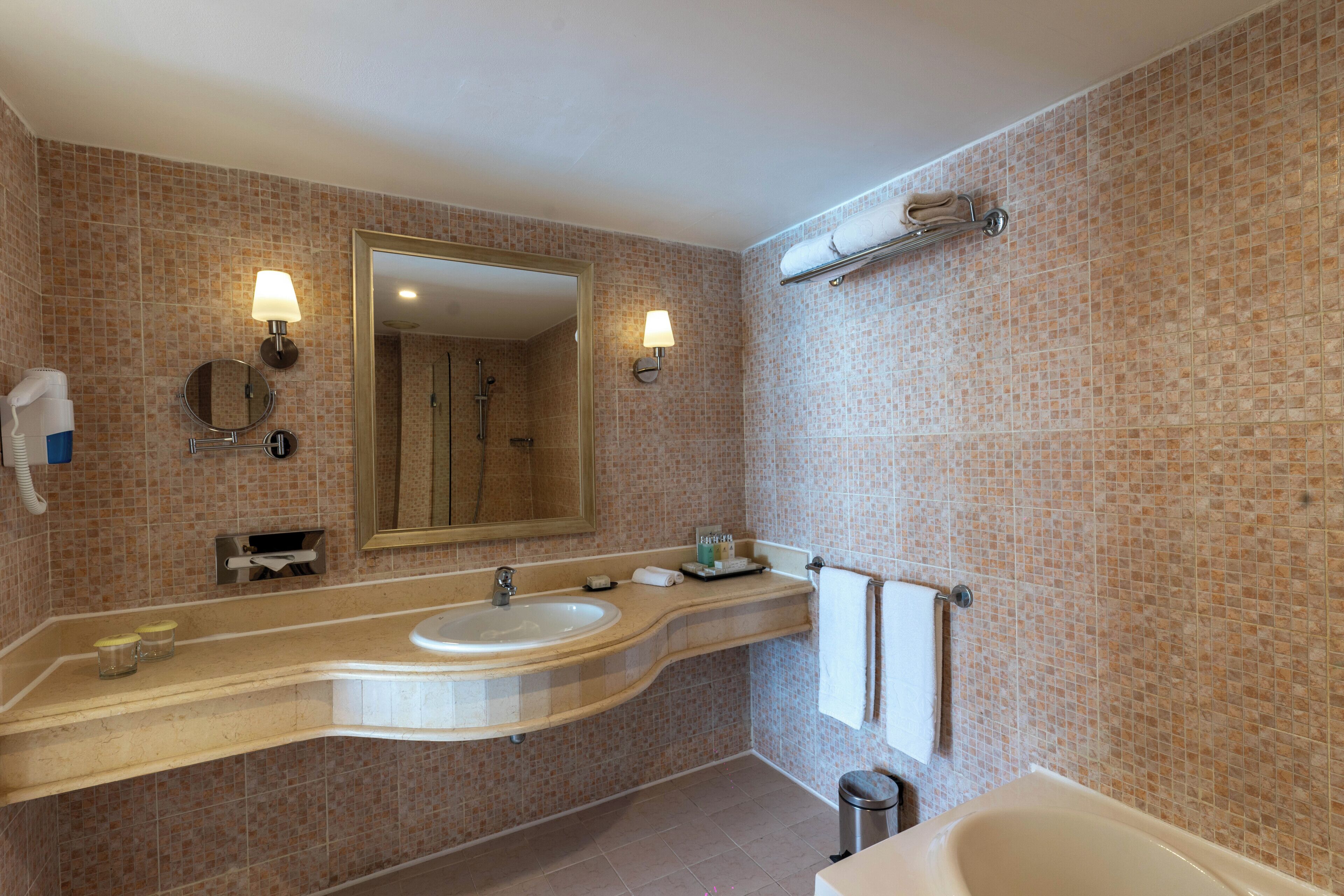 A bathroom with a sink, mirror, towel rack, and a shower area.