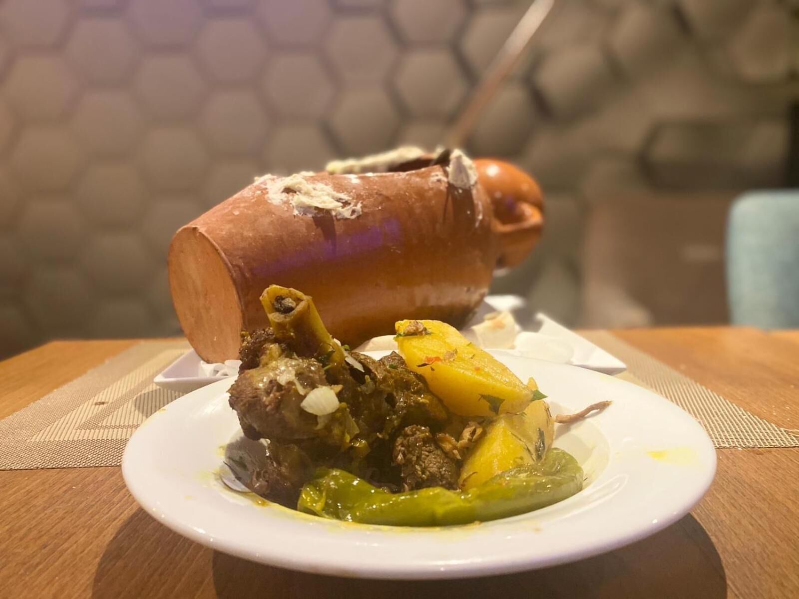 Uma perna de porco assada com osso, acompanhada de batatas e legumes num prato branco.