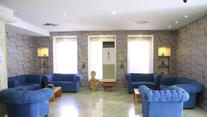 Un'ampia stanza con quattro divani blu disposti a semicerchio, un pavimento in marmo e un busto decorativo al centro.