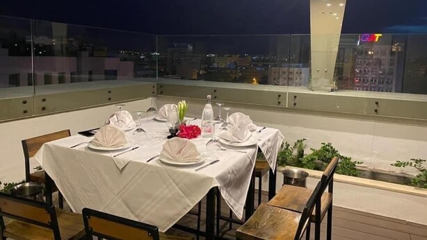 Area ristoro sul tetto con tavolo apparecchiato per quattro persone, circondata da parapetti in vetro e con vista sulla città.