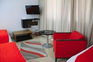 A hotel room with a TV, a small table, a red chair, and a sofa. - Hotel Le Pacha (Tunis)