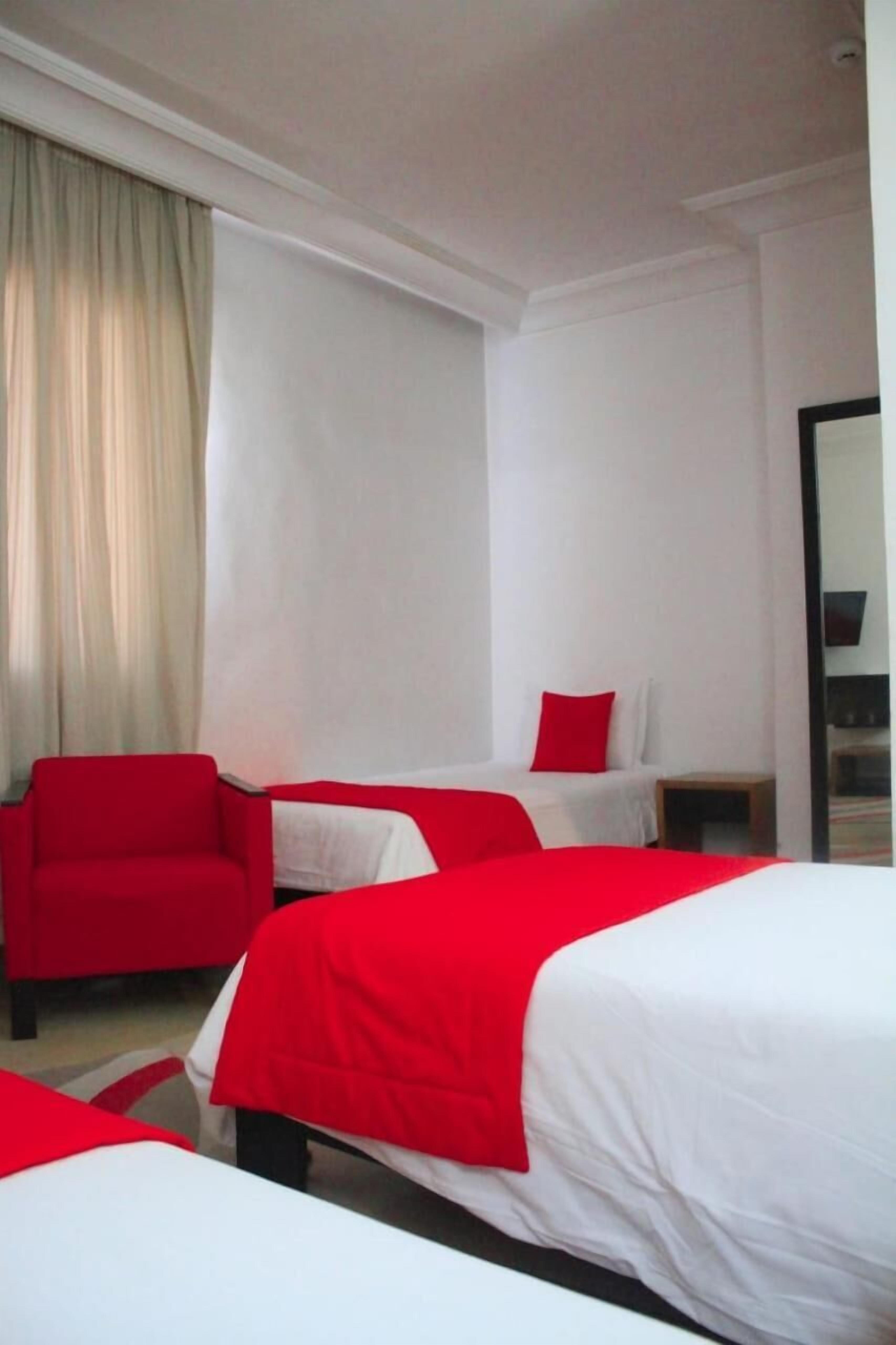 Una habitación de hotel con dos camas, un sillón rojo y un espejo grande.