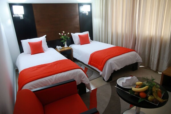 A hotel room with two beds, each with white bedding and red accents, a small table with a fruit bowl, and a nightstand with a phone and vase. - Hotel Le Pacha (Tunis)