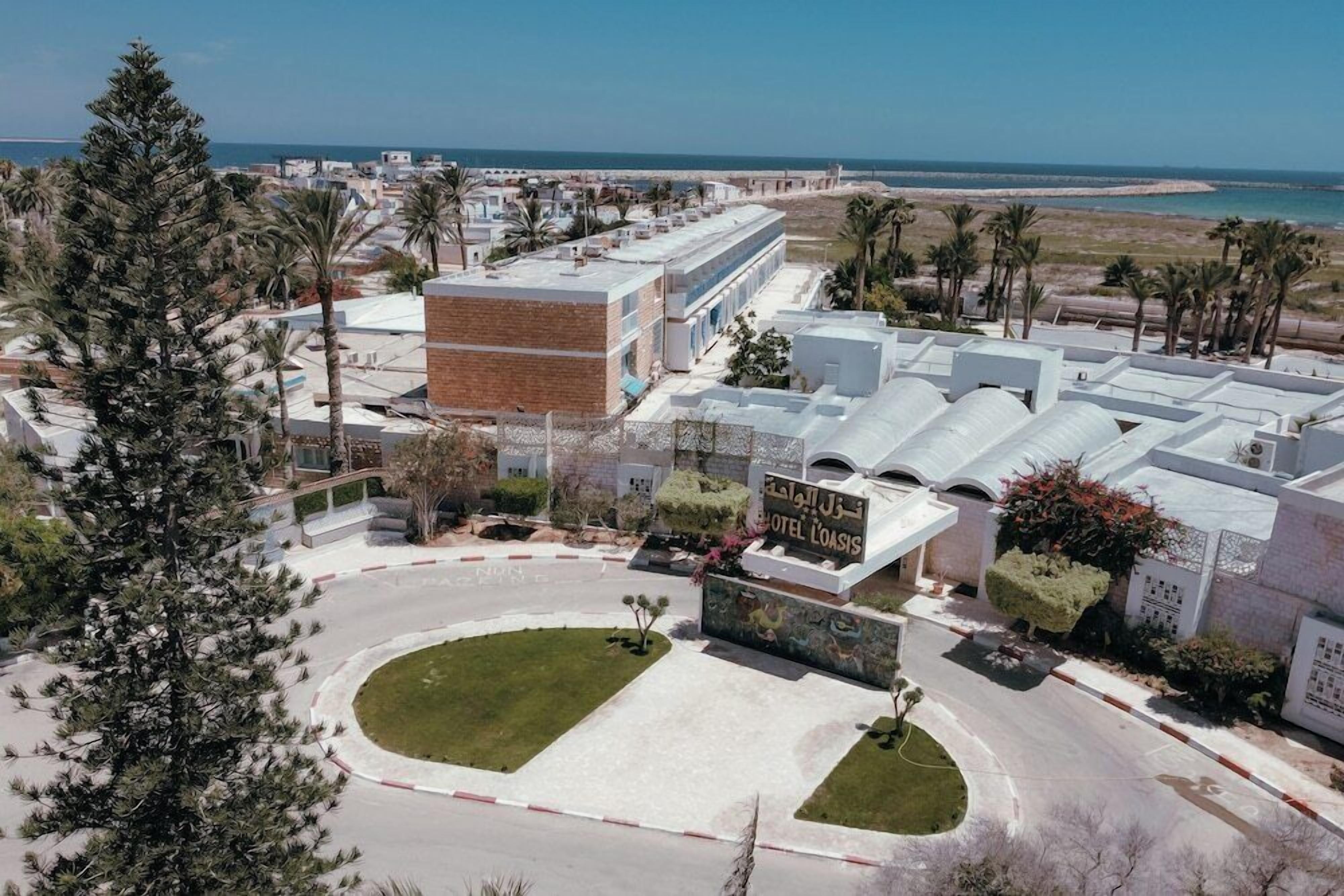 A hotel with a modern design, featuring a central courtyard, multiple buildings, and a view of the beach.