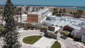 A hotel with a modern design, featuring a central courtyard, multiple buildings, and a view of the beach.