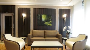Un vestíbulo moderno con un sofá, dos sillones, una mesita de centro y un cuadro de un bosque en la pared.