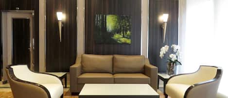 Un vestíbulo moderno con un sofá, dos sillones, una mesita de centro y un cuadro de un bosque en la pared.